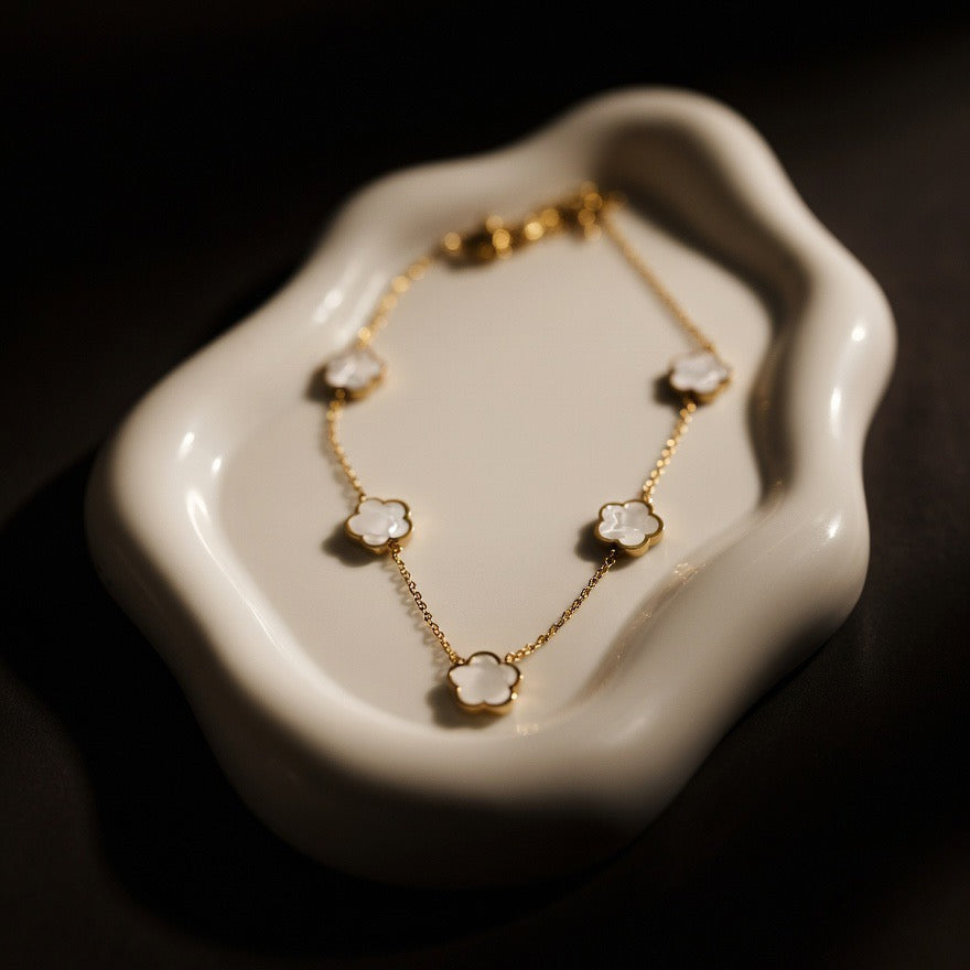 Gold necklace with floral pendants on a white dish against a dark background